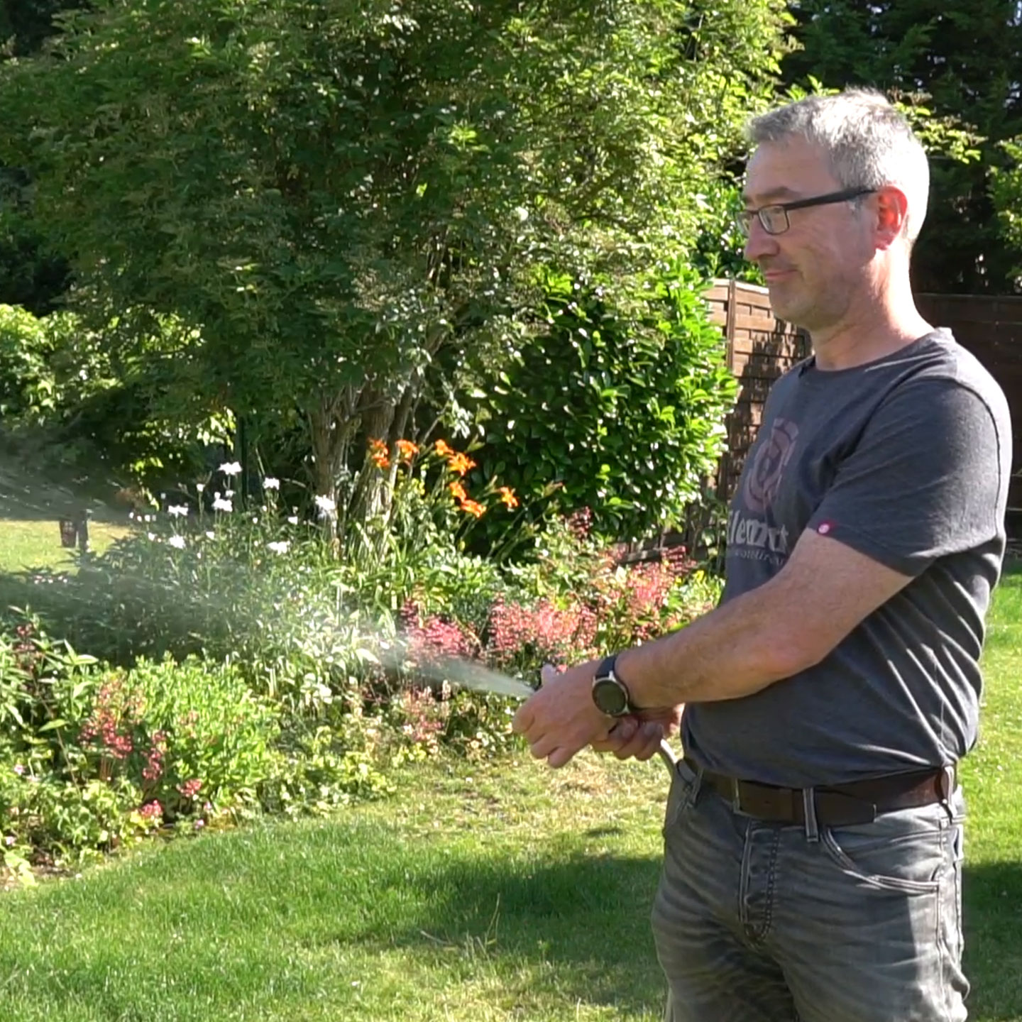 Mann bewässert Garten mit Schlauch