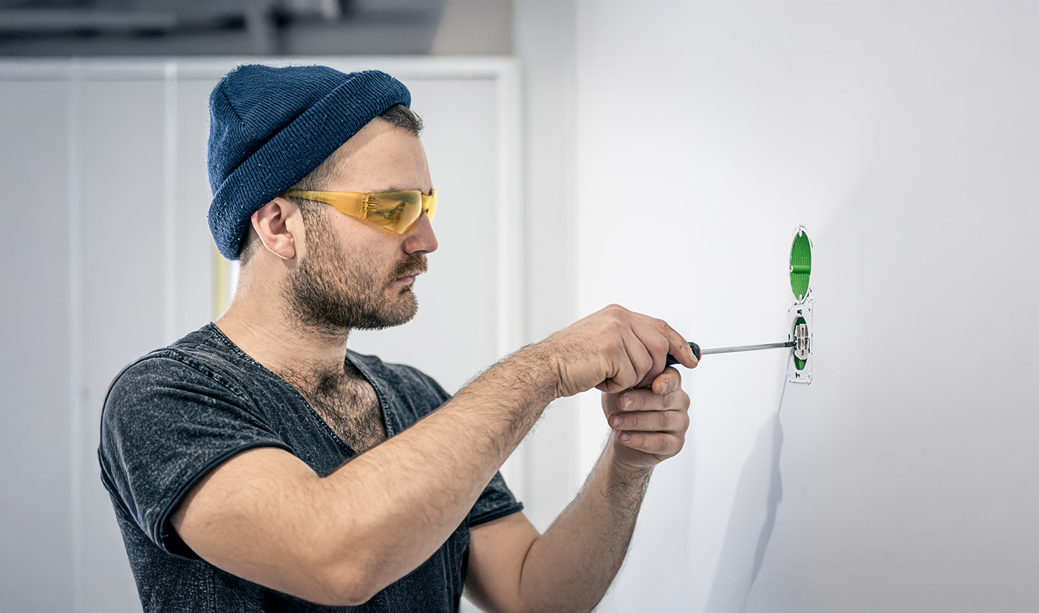 Mann mit Schutzbrille montiert Steckdose mit Schraubendreher