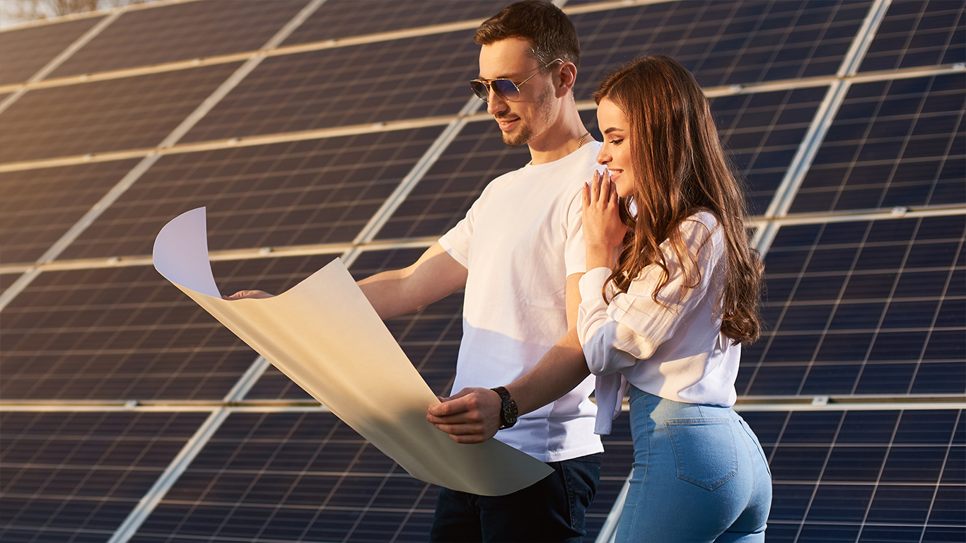 junges Paar steht mit einem Planpapier vor einem großen PV-Freilandsystem